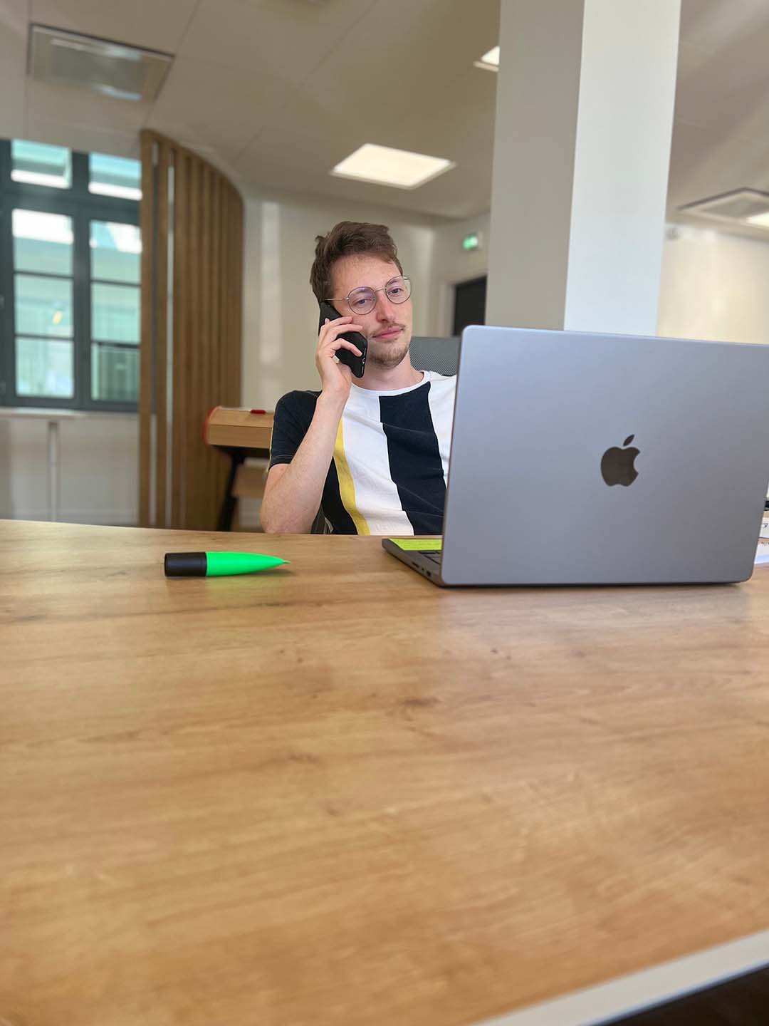 Julien de 3COM-médias, assis au bureau entrain de téléphoner devant son ordinateur