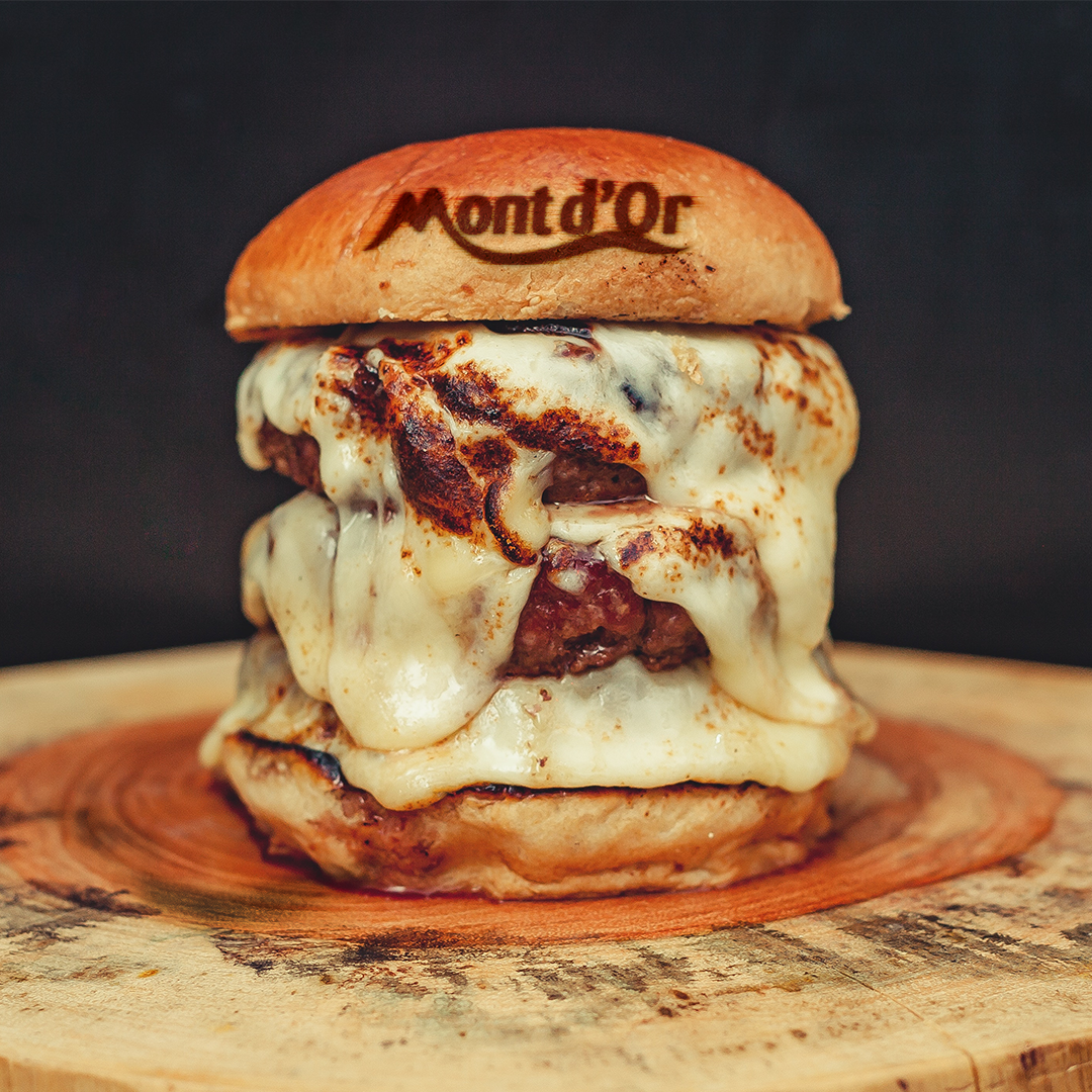 Photographie d'un burger gourmand, plein de fromage et une incrustation "Mont d'or" sur le pain